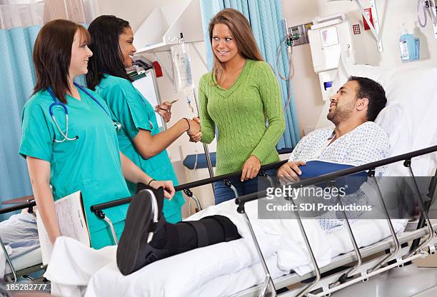 nurses greeting injured patient's spouse in hospital recovery room - woman in broken shoe heel stockfoto's en -beelden
