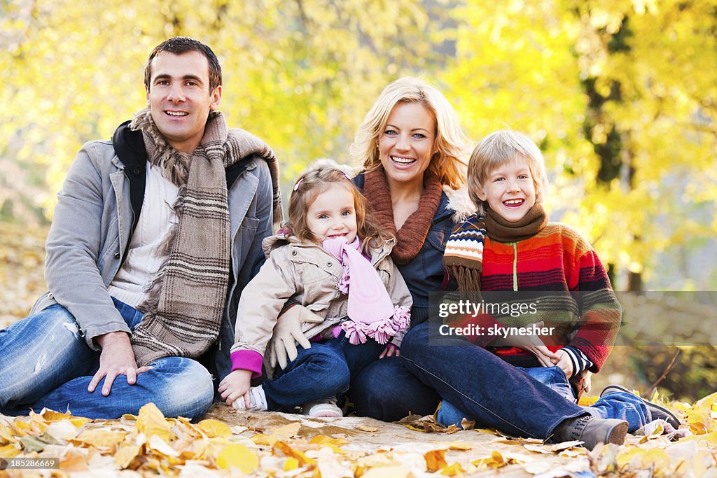 L'ambiance joyeuse famille assis parmi les feuilles dans le parc.