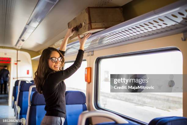 young woman putting her backpack on luggage rack in a train - luggage rack stock pictures, royalty-free photos & images