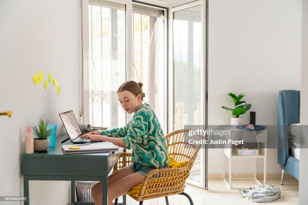 Young girl (circa 12 years old) doing her homework from a desk in her bedroom
