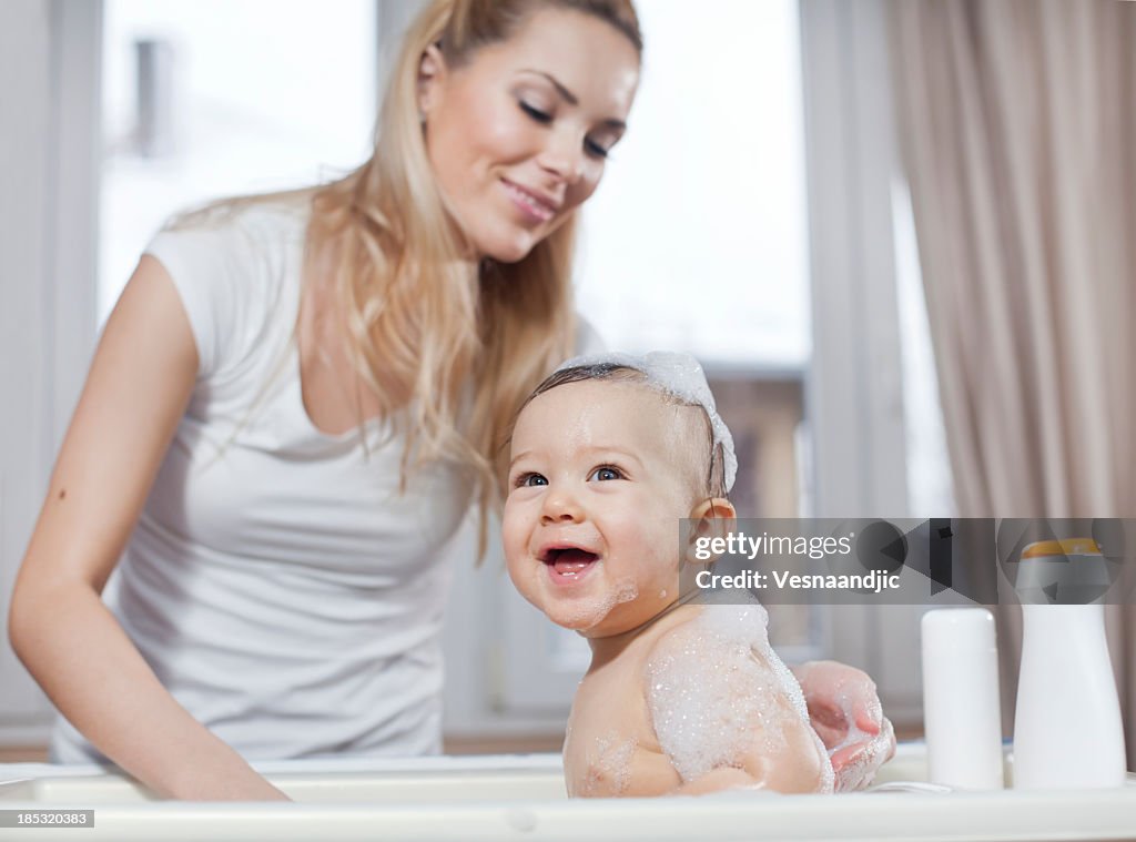 Woman bathing happy baby with foam on his head and arm
