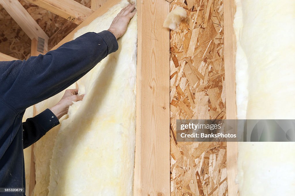 Worker Installing Fiberglass Batt Insulation between Wall Studs