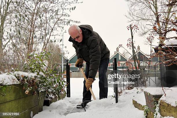 senior man removes snow - winterdienst stockfoto's en -beelden