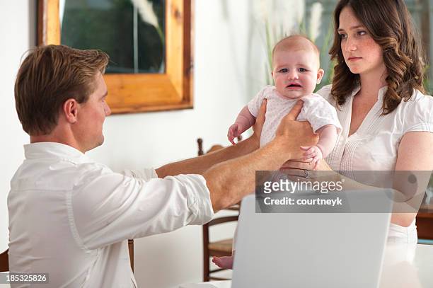 frustrated father giving a crying baby to his wife - parents arguing stock pictures, royalty-free photos & images