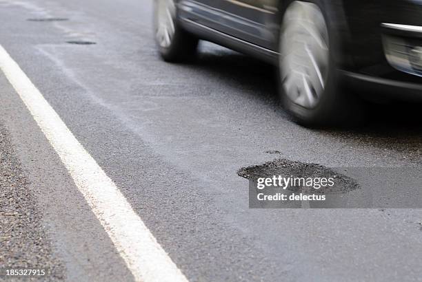 pothole on the road next to a driving car - car on road stock pictures, royalty-free photos & images