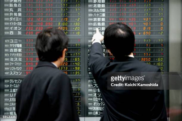 Men look at an electronic stock board March 17, 2003 in Tokyo, Japan. The Nikkei Stock Average decreased 131.05 points, closing at 7,871.64, slipping...