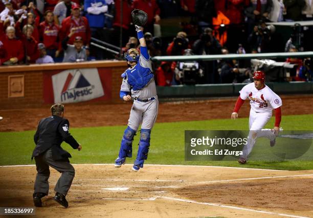Catcher A.J. Ellis of the Los Angeles Dodgers leaps after the ball thrown by Yasiel Puig as David Freese of the St. Louis Cardinals comes around to...
