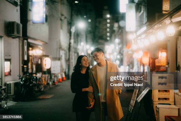 happy couple in tokyo backstreet alley at night with izakaya in winter - asiático de asia sudoriental fotografías e imágenes de stock