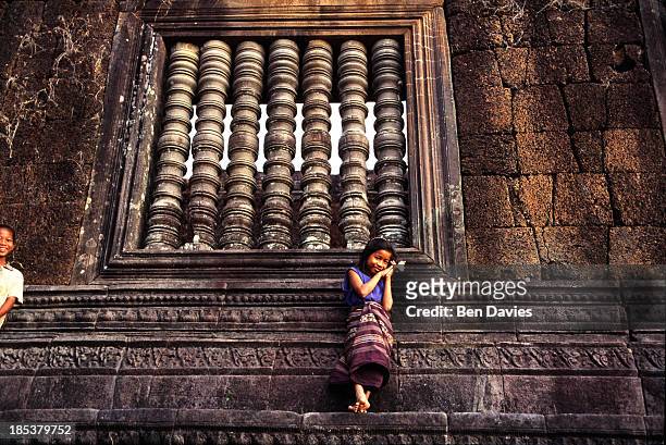 Girl dressed in traditional costume with a flower and incense sticks poses in front of the ruins of the magnificent Hindu Khmer temple of Wat Phu in...
