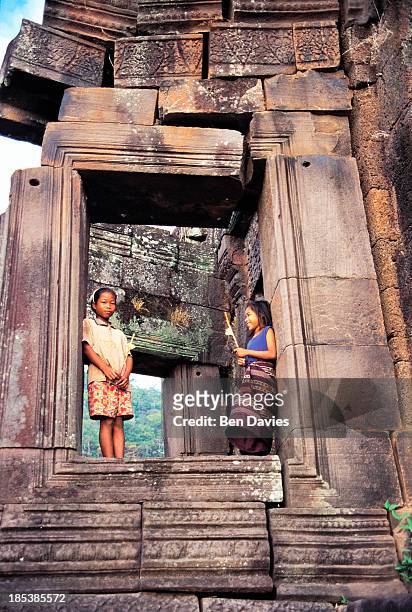Two children clutching flowers and incense sticks pose in front of the ancient ruins of the Hindu Khmer temple of Wat Phu in Champasak Province...