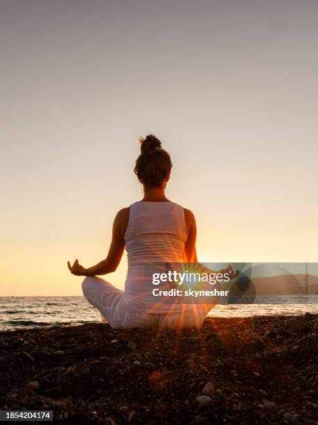 back view of a woman exercising yoga on the beach at sunset. - lotuspositie stockfoto's en -beelden