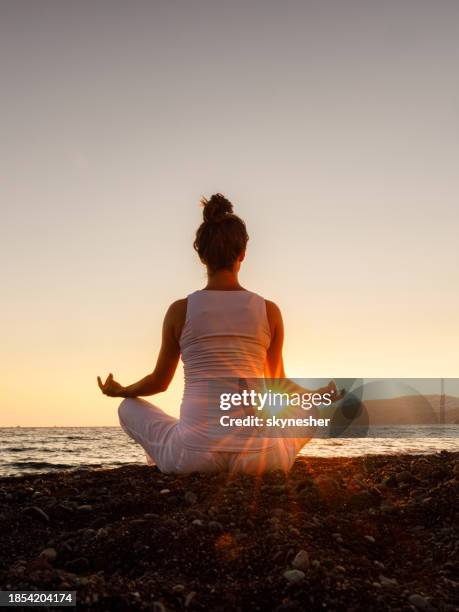 back view of a woman exercising yoga on the beach at sunset. - budismo imagens e fotografias de stock