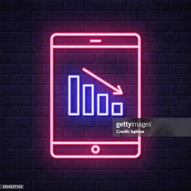 decreasing chart on tablet pc. glowing neon icon on brick wall background - decrease infographic stock illustrations