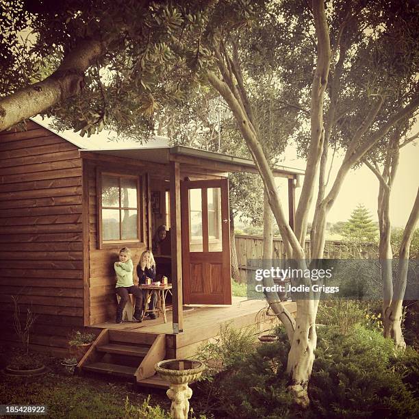 children sitting on verandah of small wooden house - jodie griggs stock pictures, royalty-free photos & images
