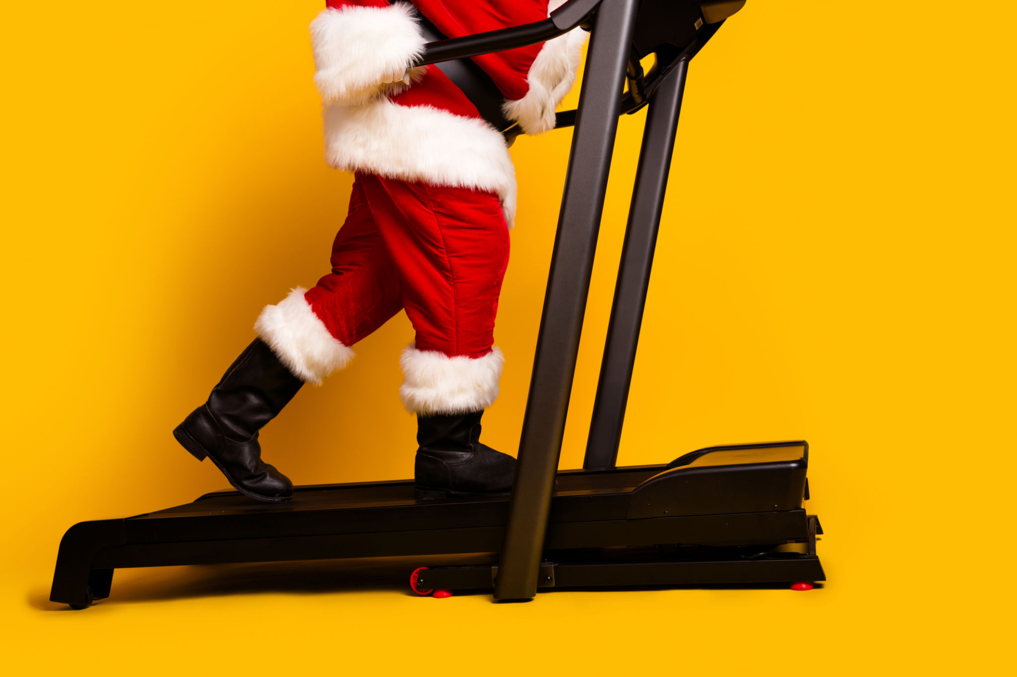 Profile side cropped photo of elderly man santa claus in traditional shoes going on treadmill isolated yellow color background Profile side cropped photo of elderly man santa claus in traditional shoes going on treadmill isolated yellow color background