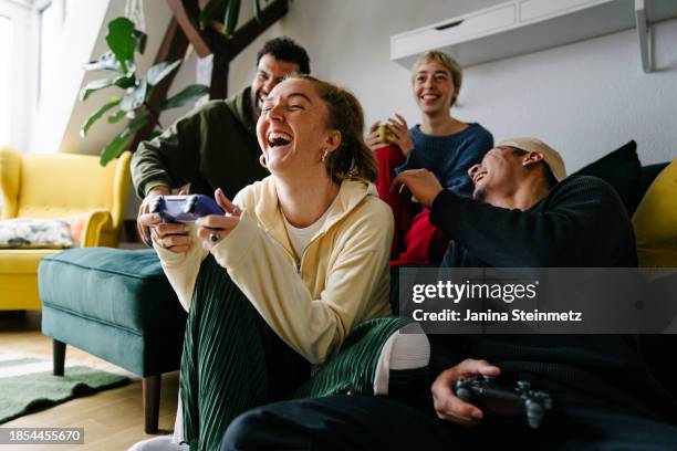 portrait of a group of gen z relaxing at home and having fun playing with controllers - videospel stockfoto's en -beelden