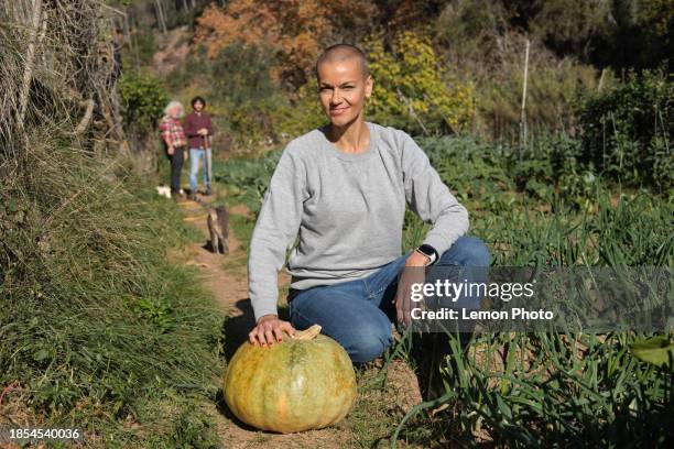 medium shot of a happy caucasian generation x female with a giant pumpkin in a community garden looking at the camera and smiling - giant camera stock pictures, royalty-free photos & images