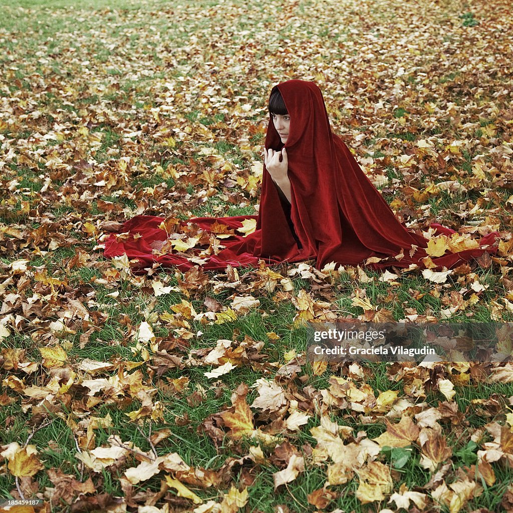 Girl covered with red cape in autumnal field