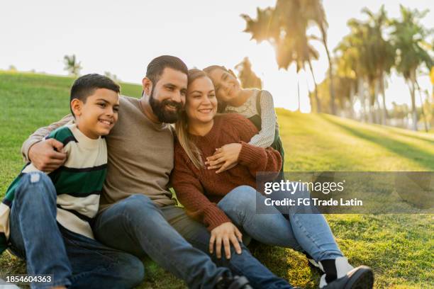 family sitting on ground in public park - park family sunset stock pictures, royalty-free photos & images