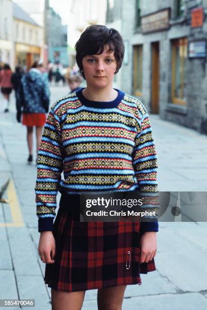 1st JUNE: A young woman poses wearing a Fair Isle sweater and kilt in Lerwick, Shetland Islands in June 1970.