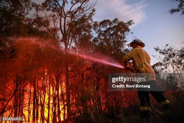 Rural Fire Service firefighter attempt to extinguish a bush fire at West Wallsend on December 14, 2023 in Newcastle, Australia. Several fast-moving...