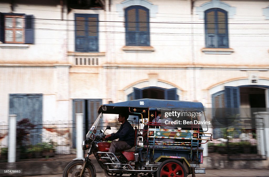 A motorcycle taxi passes in front of the imposing facade of...