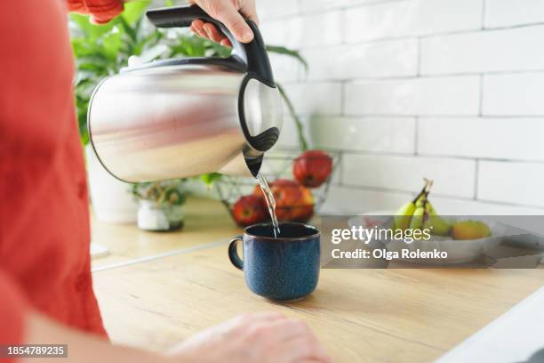 unrecognizable woman pouring hot water into a mug from a kettle in the kitchen - kettle stock pictures, royalty-free photos & images