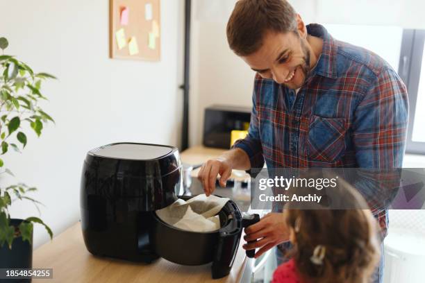 kleines mädchen, das mit ihrem vater in der küche das frühstück zubereitet - airfryer stock-fotos und bilder