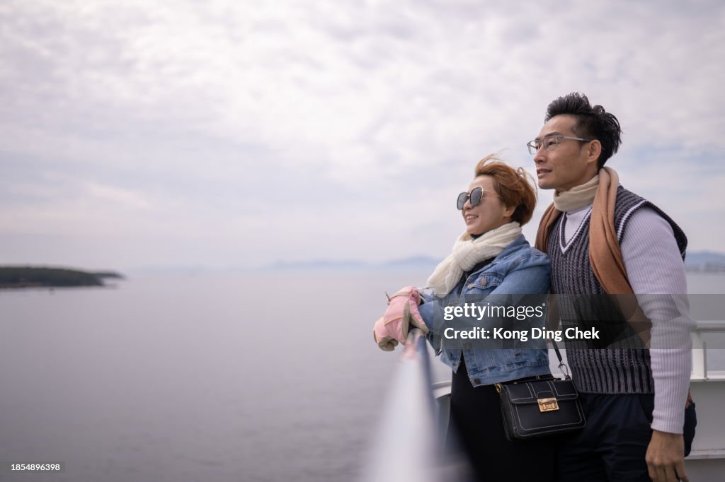 Asian Chinese couple leaning against railing on ferry enjoy their holiday in Japan