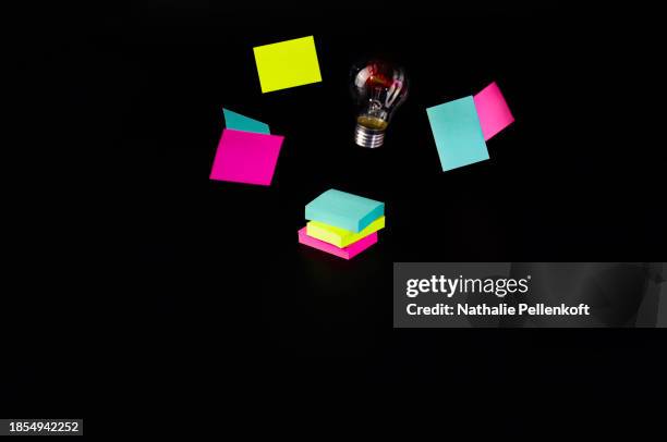 high angle view of multi colored sticky notes and light bulb on black background - nathalie pellenkoft stock pictures, royalty-free photos & images