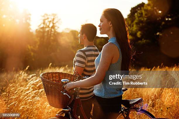 man and woman with bikes in field at sunset. - two people looking at view stock pictures, royalty-free photos & images