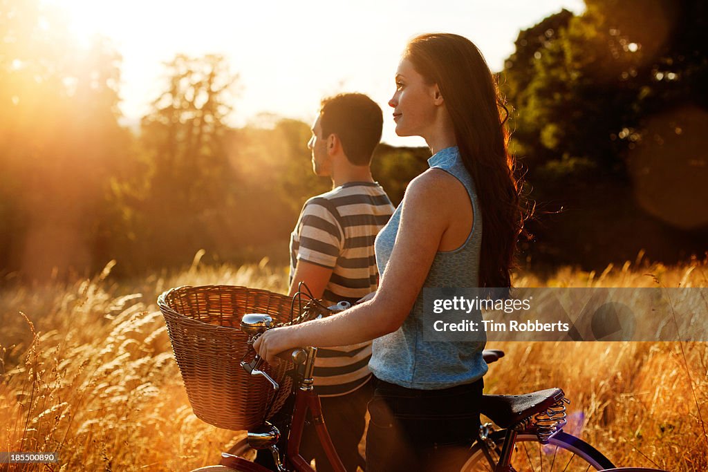 Man and woman with bikes in field at sunset.