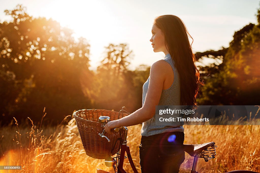 Woman with bike in field at sunset.