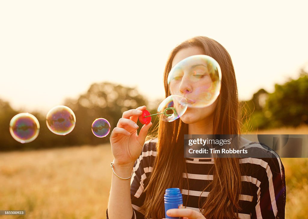 Young woman blowing bubbles in field.