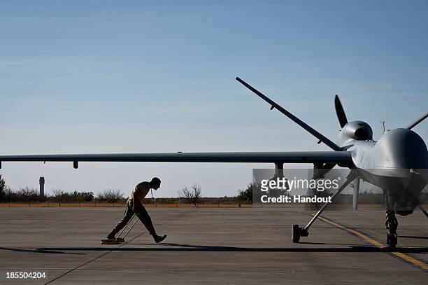 In this handout provided by the U.S. Air Force, after taxiing in an MQ-9 Reaper, Airman 1st Class Jon Mann walks under a Reaper's wing to place wheel...