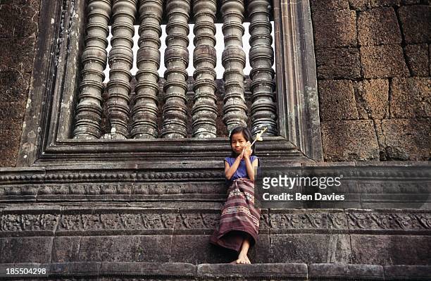 Girl dressed in traditional costume with a flower and incense sticks poses in front of the ruins of the magnificent Hindu Khmer temple of Wat Phu in...