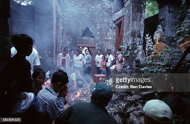 The Buddhist faithful worship in front of a statue of the Buddha inside the ruins of the Hindu Khmer temple of Wat Phu in Champassak province, Laos,...