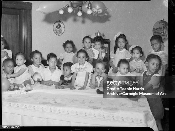 Jackie Ann Hamilton surrounded by boys and girls gathered behind table with birthday cake patterned tablecloth in Hamilton's home, Anaheim street,...
