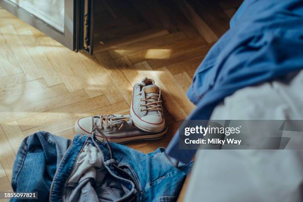 jeans and sneakers lie on the parquet floor near the bed. mess in the room. - spogliarsi foto e immagini stock