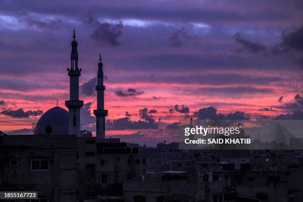 The sky is illuminated red at sunset behind mosque minarets in Rafah in the southern Gaza Strip near the border with Egypt on December 17, 2023 amid...