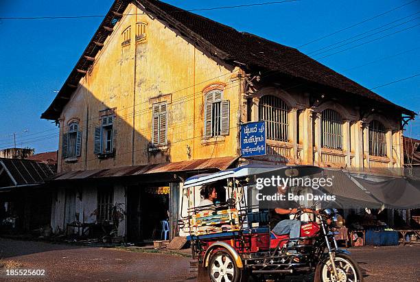 Motorcycle taxi passes in front of the imposing facade of a French colonial building in Savannakhet in Southern Laos. Like Vientiane and Luang...