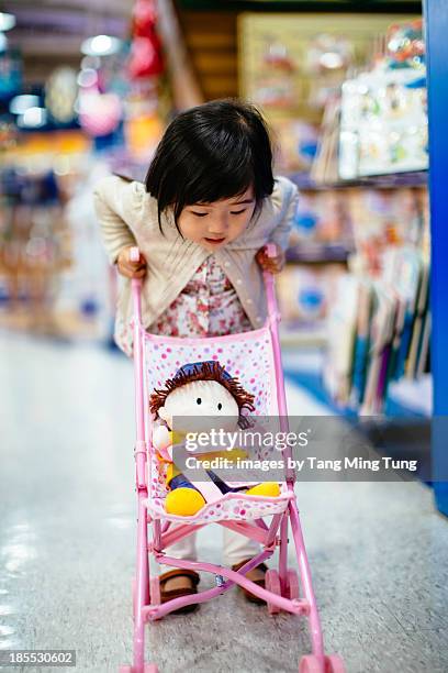 toddler girl pushing a toy stroller in toy shop - doll fotografías e imágenes de stock