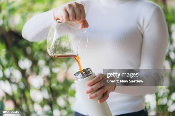 close up hand of woman pouring hot coffee into thermos at home. - laboratoriumglas stockfoto's en -beelden