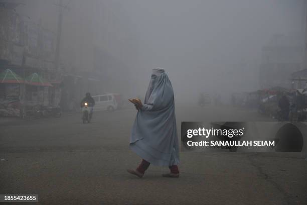 An Afghan burqa-clad woman walks across a road in Kandahar on December 17, 2023.