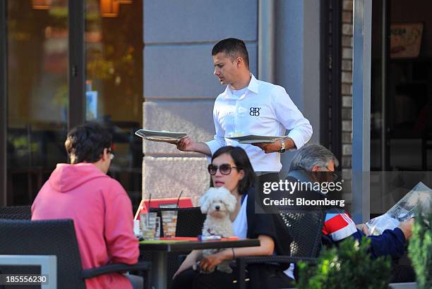 Waiter delivers food to waiting customers seated at an outdoor cafe in Belgrade, Serbia, on Sunday, Oct. 20, 2013. Serbia's government revealed a...