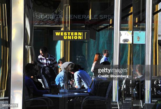 Customers at an outdoor cafe are seen reflected in the window of a Western Union Co. Branch in Belgrade, Serbia, on Sunday, Oct. 20, 2013. Serbia's...