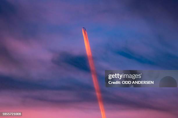 The setting sun colors the vapour trail of a plane above Berlin on December 17, 2023. The German capital experienced mild and partly clear weather on...