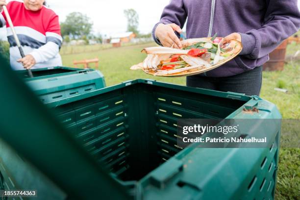 a young female placing organic waste from plastic container into a compost bin in rural area. embracing sustainable and eco-friendly lifestyle - biodegradable stock pictures, royalty-free photos & images