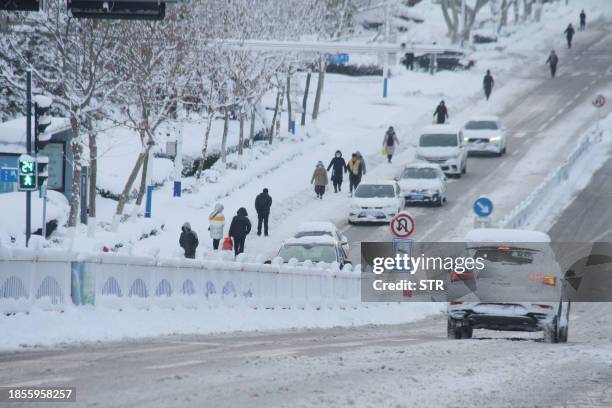 In this photo taken on December 16 residents walk on a road during a snowfall in Weihai, in China's eastern Shandong province. / China OUT