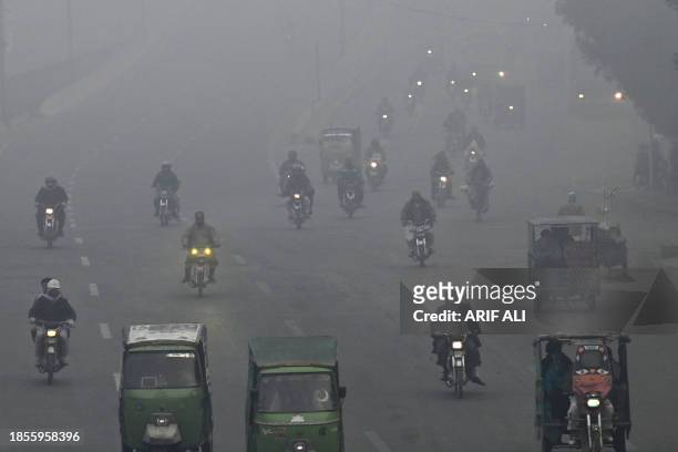 Commuters make their way along a street amid dense smog in Lahore on December 18, 2023.